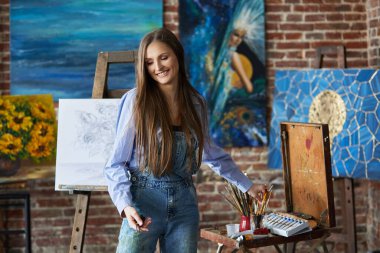 Sanat atölyesinde genç, gülümseyen kadın sanatçının portresi. Resim fırçası tutan bir ressam. Yaratıcı süreç, rahatlama, rahatlama, hobi, stres yönetimi
