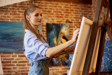 Yağlı boya tabloları ve sanat fırçasıyla tuvale resim yapan genç ve güzel bir kadın sanatçı. Ressam sanat stüdyosunda sanat eseri yaratıyor. Rahatlama, rahatlama, hobi, stres yönetimi