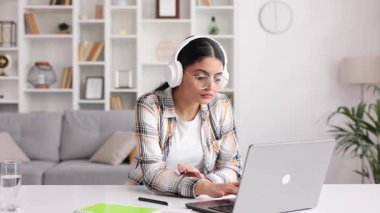 Beyaz kulaklıklı tatmin olmuş Hintli kız e-postalarını kontrol ediyor ve iyi haberlerle mutlu. Kanepede dans eden genç bir kadın zaferi kutluyor, elinde kalemlerle.