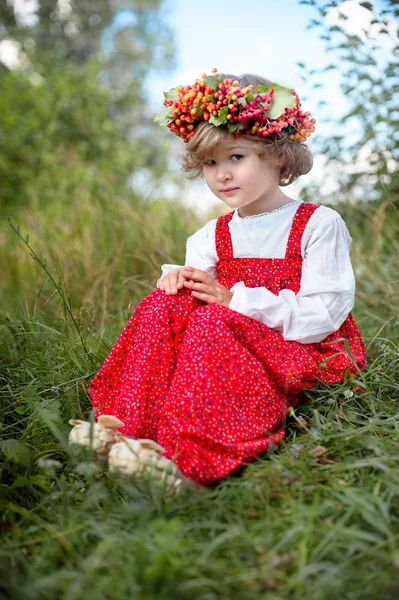 Menina bonita em vestido vermelho sentado na grama com um ramo o — Fotografia de Stock