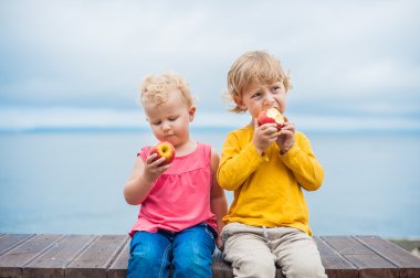 Yeni yürümeye başlayan çocuklar erkek ve kız bir bankta oturan bir elma yemek