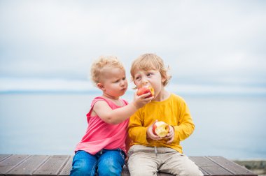 Yeni yürümeye başlayan çocuklar erkek ve kız bir bankta oturan bir elma yemek