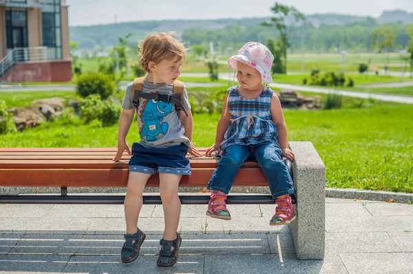 Kleine Jungen und Mädchen sitzen auf der Bank im Sommerpark — Stockfoto