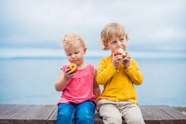 Хлопчик і дівчинка, що сидить на лавці, їдять яблуко — стокове фото