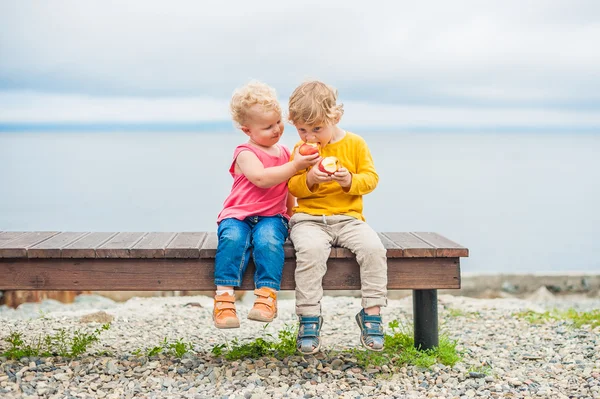 幼児の男の子と女の子がベンチに座ってリンゴを食べる — ストック写真