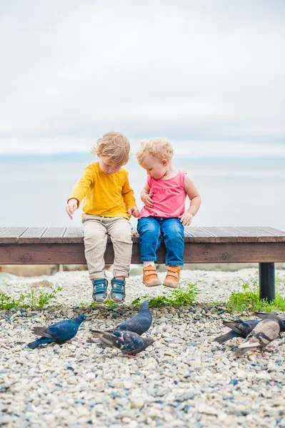 Niño y niña sentados cerca del mar alimentaban a las palomas con pan — Foto de Stock