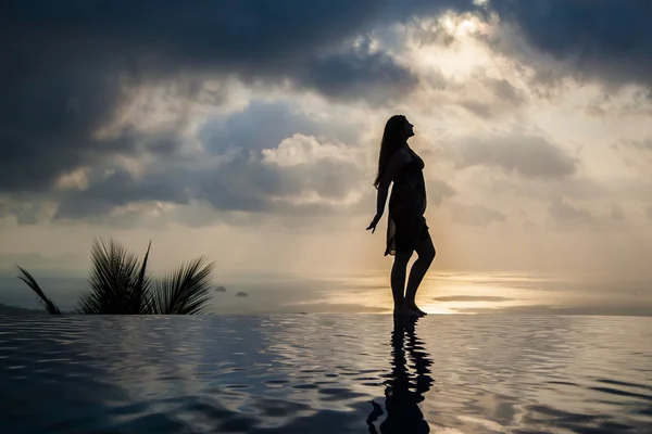 Silhueta de uma mulher na piscina panorâmica ao pôr do sol — Fotografia de Stock