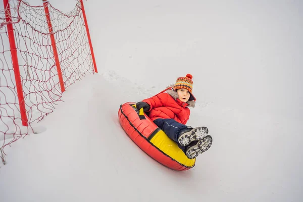 Das Kind hat Spaß auf der Schneekanone. Junge reitet auf einem Schlauch. Winterspaß für Kinder — Stockfoto