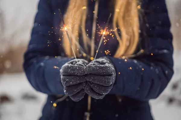 Jiskry v ženských rukou na pozadí sněžení. Koncept Vánoc a Nového roku — Stock fotografie