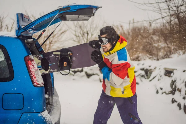 The snowboard does not fit into the car. A snowboarder is trying to stick a snowboard into a car. Humor, fun — Stock Photo, Image