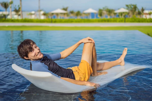 Расслабься в бассейне. Молодой и успешный человек, лежащий на шезлонге и загаре в бассейне отеля — стоковое фото
