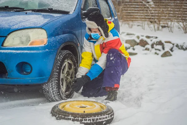 Зимова аварія на дорозі. Чоловік змінює колесо під час снігопаду через коронавірус COVID-19. Зимові проблеми — стокове фото