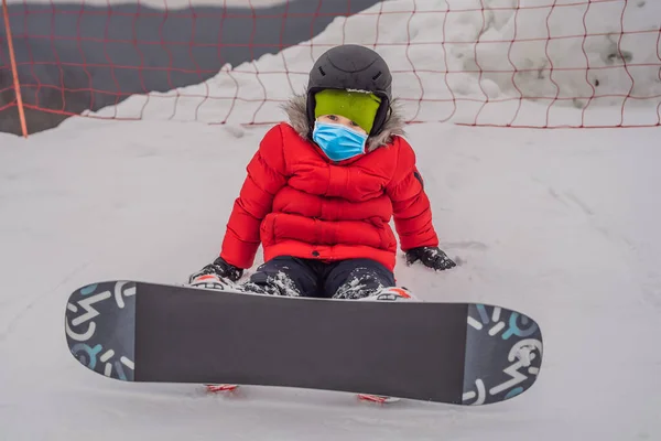 Petit garçon mignon snowboard portant un masque médical pendant le coronavirus COVID-19. Activités pour les enfants en hiver. Sport d'hiver pour enfants. Mode de vie — Photo
