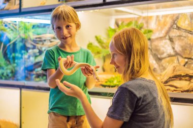 Gülümseyen çocuk ve annesi pitonu ellerinde tutuyorlar.