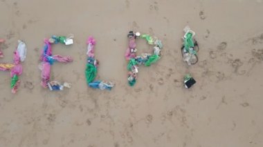 Kumlu bir plajda çöpten yapılmış bir harfin havadan çekilmiş fotoğrafı. Üzgün bir ekolojik gönüllü kumların üzerinde harflerin yanında yatıyor. Plastik kirliliğini durdur