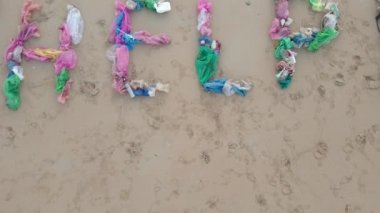 Kumlu bir plajda çöpten yapılmış bir harfin havadan çekilmiş fotoğrafı. Üzgün bir ekolojik gönüllü kumların üzerinde harflerin yanında yatıyor. Plastik kirliliğini durdur