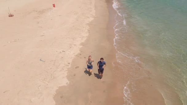 Prise de vue aérienne d'un jeune homme et d'une jeune femme faisant du jogging sur une belle plage. Concept de mode de vie sain et de sport — Video