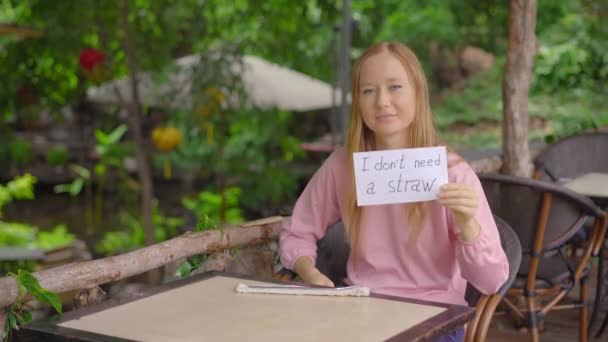 In a cafe, a young woman refuses to take a single-use plastic drinking straw. She is holding a paper with a sign I DONT NEED A STRAW. Concept of reducing the use single plastic — Stock Video