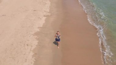 Güzel bir plajda koşan genç bir kadının hava görüntüsü. Sağlıklı yaşam tarzı ve spor anlayışı