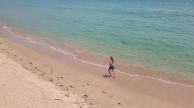 Güzel bir plajda koşan genç bir kadının hava görüntüsü. Sağlıklı yaşam tarzı ve spor anlayışı