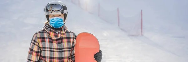 Γυναίκα snowboarder σε μια ηλιόλουστη μέρα του χειμώνα σε ένα χιονοδρομικό κέντρο φορώντας μια ιατρική μάσκα κατά τη διάρκεια COVID-19 coronavirus BANNER, LONG FORMAT — Φωτογραφία Αρχείου