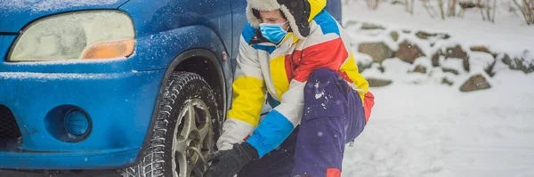 Accidente de invierno en la carretera. Un hombre cambia una rueda durante una nevada usando máscaras médicas debido al coronavirus COVID-19. Problemas de invierno BANNER, FORMATO LARGO —  Fotos de Stock