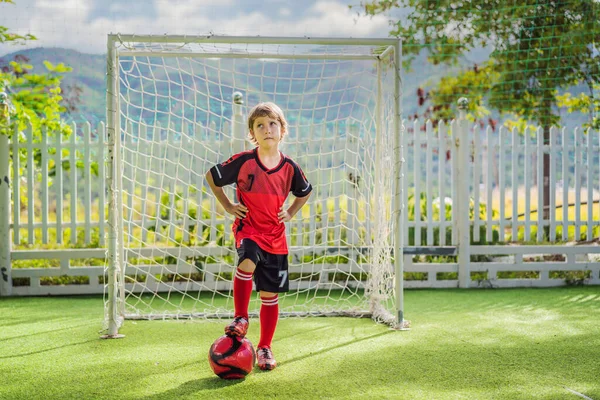 Kleiner süßer Junge in roter Fußballuniform, der Fußball spielt, Fußball auf dem Feld, im Freien. Aktives Kind, das mit Kindern oder Vater Sport treibt, lächelnder fröhlicher Junge, der Spaß im Sommer hat — Stockfoto