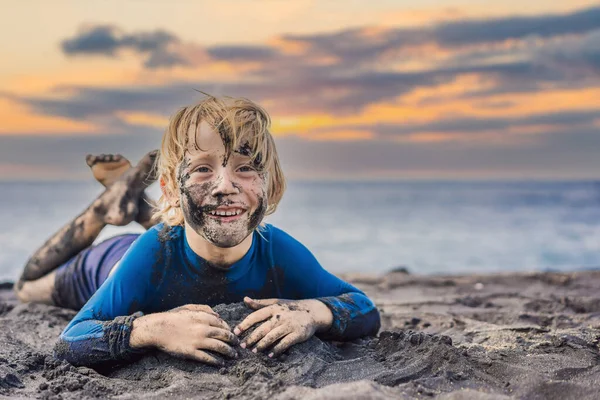 11.11 Concetto di Venerdì nero. Ragazzo sorridente con la faccia nera sporco seduto e giocare sulla spiaggia di sabbia nera. Vacanze estive con bambini. Venerdì nero, vendita di tour e biglietti aerei o merci — Foto Stock