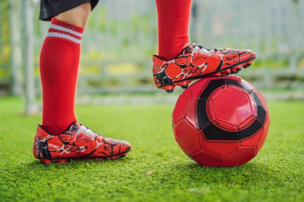 A kis cuki fiú piros foci egyenruhában focizik, focizik a pályán, a szabadban. Aktív gyermek sportolás gyerekekkel vagy apával, mosolygós boldog fiú szórakozás nyáron — Stock Fotó