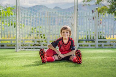 Kırmızı futbol forması giyen, futbol oynayan, sahada, dışarıda futbol oynayan tatlı bir çocuk. Aktif çocuk çocuklarla ya da babayla spor yapıyor, gülen mutlu çocuk yazın eğleniyor.