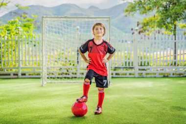 Kırmızı futbol forması giyen, futbol oynayan, sahada, dışarıda futbol oynayan tatlı bir çocuk. Aktif çocuk çocuklarla ya da babayla spor yapıyor, gülen mutlu çocuk yazın eğleniyor.