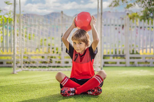 Little cute kid boy in red football uniform playing soccer, football on field, outdoors. Active child making sports with kids or father, Smiling happy boy having fun in summer — Stock Photo, Image