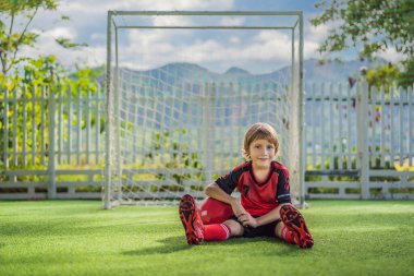 Kırmızı futbol forması giyen, futbol oynayan, sahada, dışarıda futbol oynayan tatlı bir çocuk. Aktif çocuk çocuklarla ya da babayla spor yapıyor, gülen mutlu çocuk yazın eğleniyor.