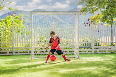 Kırmızı futbol forması giyen, futbol oynayan, sahada, dışarıda futbol oynayan tatlı bir çocuk. Aktif çocuk çocuklarla ya da babayla spor yapıyor, gülen mutlu çocuk yazın eğleniyor.
