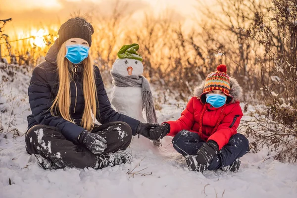 코로나 바이러스 (COVID-19 coronavirus) 중에 따뜻 한 옷을 입은 행복 한 가족. 어머니와 아들이 야외에서 눈 사람을 만들고 있습니다. 겨울 활동의 개념 — 스톡 사진