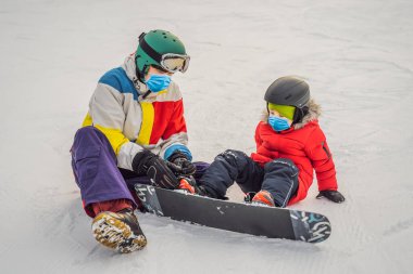 Snowboard eğitmeni bir çocuğa COVID-19 Coronavirus sırasında tıbbi maske takarak snowboard yapmayı öğretiyor. Kışın çocuklar için etkinlikler. Çocuklar kış sporu. Yaşam biçimi