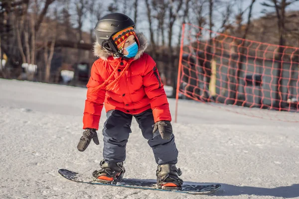 Petit garçon mignon snowboard portant un masque médical pendant le coronavirus COVID-19. Activités pour les enfants en hiver. Sport d'hiver pour enfants. Mode de vie — Photo