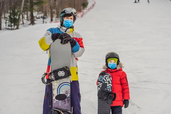 Un moniteur de snowboard apprend à un garçon à faire du snowboard en portant un masque médical pendant le coronavirus COVID-19. Activités pour les enfants en hiver. Sport d'hiver pour enfants. Mode de vie — Photo