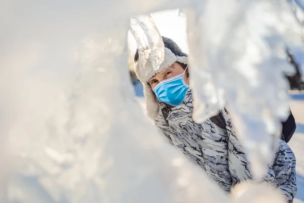 Mladý muž s lékařskou maskou během COVID-19 coronavirus mezi ledem v zimě venku. Zimní koncept — Stock fotografie