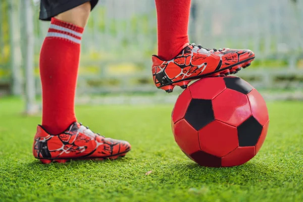 Menino bonito em uniforme de futebol vermelho jogando futebol, futebol no campo, ao ar livre. Criança ativa fazendo esportes com crianças ou pai, sorrindo menino feliz se divertindo no verão — Fotografia de Stock