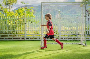 Kırmızı futbol forması giyen, futbol oynayan, sahada, dışarıda futbol oynayan tatlı bir çocuk. Aktif çocuk çocuklarla ya da babayla spor yapıyor, gülen mutlu çocuk yazın eğleniyor.