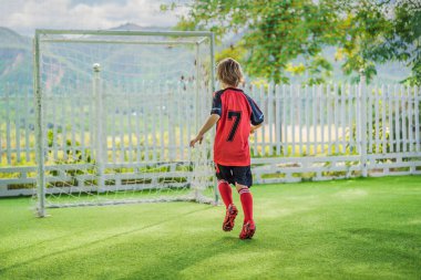 Kırmızı futbol forması giyen, futbol oynayan, sahada, dışarıda futbol oynayan tatlı bir çocuk. Aktif çocuk çocuklarla ya da babayla spor yapıyor, gülen mutlu çocuk yazın eğleniyor.