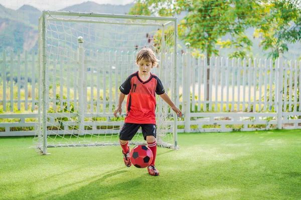 Little cute kid boy in red football uniform playing soccer, football on field, outdoors. Active child making sports with kids or father, Smiling happy boy having fun in summer — Stock Photo, Image