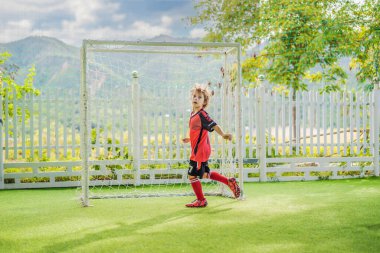 Kırmızı futbol forması giyen, futbol oynayan, sahada, dışarıda futbol oynayan tatlı bir çocuk. Aktif çocuk çocuklarla ya da babayla spor yapıyor, gülen mutlu çocuk yazın eğleniyor.