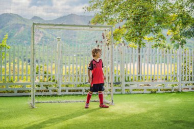 Kırmızı futbol forması giyen, futbol oynayan, sahada, dışarıda futbol oynayan tatlı bir çocuk. Aktif çocuk çocuklarla ya da babayla spor yapıyor, gülen mutlu çocuk yazın eğleniyor.