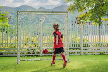 Kırmızı futbol forması giyen, futbol oynayan, sahada, dışarıda futbol oynayan tatlı bir çocuk. Aktif çocuk çocuklarla ya da babayla spor yapıyor, gülen mutlu çocuk yazın eğleniyor.