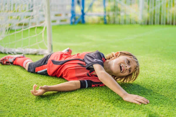 Little cute kid boy in red football uniform playing soccer, football on field, outdoors. Active child making sports with kids or father, Smiling happy boy having fun in summer — Stock Photo, Image