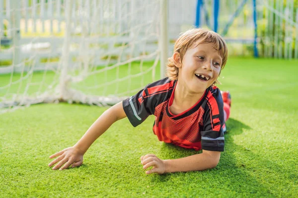 Little cute kid boy in red football uniform playing soccer, football on field, outdoors. Active child making sports with kids or father, Smiling happy boy having fun in summer — Stock Photo, Image
