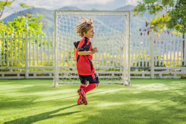 Kırmızı futbol forması giyen, futbol oynayan, sahada, dışarıda futbol oynayan tatlı bir çocuk. Aktif çocuk çocuklarla ya da babayla spor yapıyor, gülen mutlu çocuk yazın eğleniyor.