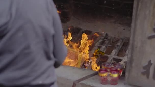 Uma pessoa queima papéis joss ou papéis ofertas em um templo budista — Vídeo de Stock